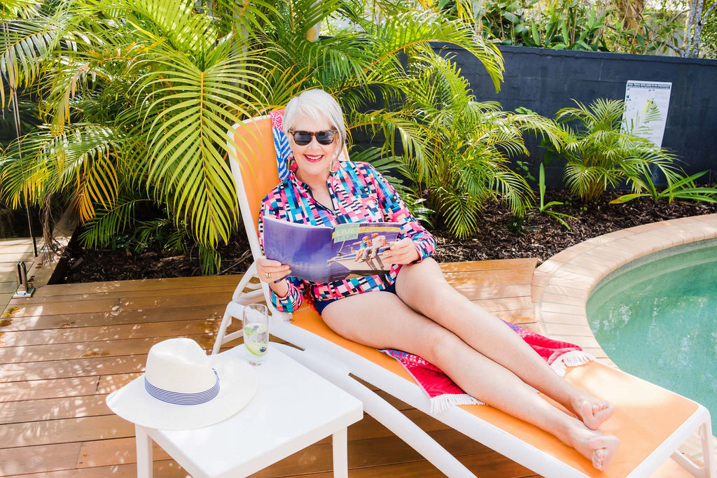 Woman lying by pool reading and wearing Capriosca Swimwear Geo Stripe Long Sleeve Rashie Navy High Waist Pant