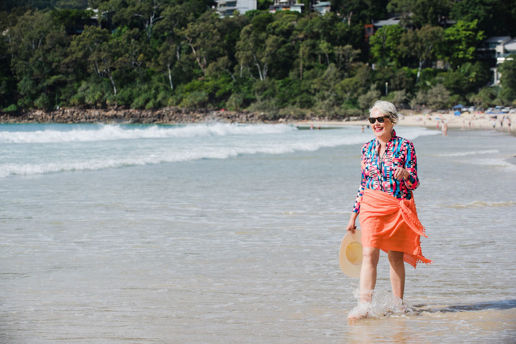 Woman walking in shallows wearing curvy swimwear long sleeve Wetsuit and Coral Sarong