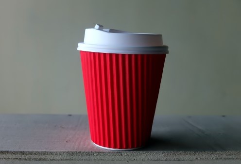 A red takeaway coffee cup with a plastic lid. Stop using these as part of your sustainable living plan.