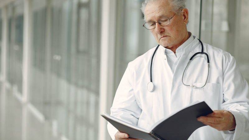 medical professional in white coat with stethoscope reading a file