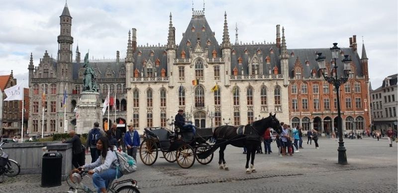 A horse and cart is surrounded by people in the Markt Square in Bruges