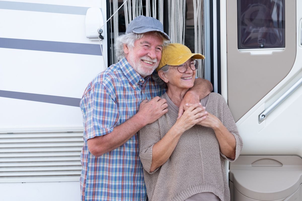 Grey nomads standing with their caravan.